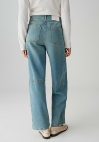 Hellblaue Denim-Jeans mit weitem Bein, Rückentaschen und sichtbaren Nähdetails, kombiniert mit einem weißen strukturierten Langarmoberteil.
