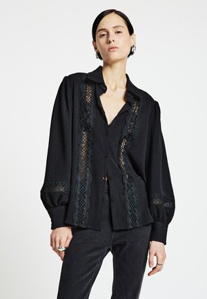 Black blouse with lace detailing along the front and sleeves, buttoned up, featuring a collared neckline and relaxed fit. Smooth fabric texture.