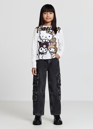 Camicia bianca a maniche lunghe con personaggi dei cartoni animati colorati e testo; abbinata a pantaloni cargo neri con molte tasche e tessuto testurizzato.