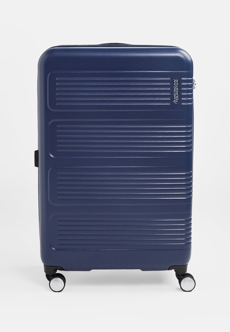 Maleta rígida de color azul marino con ranuras horizontales, textura suave, asa telescópica, cuatro ruedas y logo de la marca en el lateral.