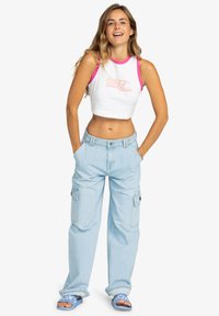 Top corto blanco sin mangas con ribetes rosas y logotipo, jeans cargo azul claro y sandalias azules, con un ajuste holgado y múltiples bolsillos.