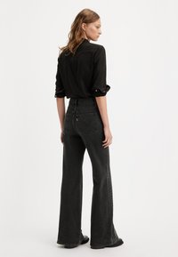 Sorte flared jeans med høj talje; tekstureret denimstof; klassiske baglommer og subtile syninger; parret med en sort skjorte.