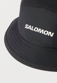 Μαύρο καπέλο τύπου bucket Salomon με εμφανείς ραφές στη γείσο, πάνω σε ουδέτερο ανοιχτό φόντο.