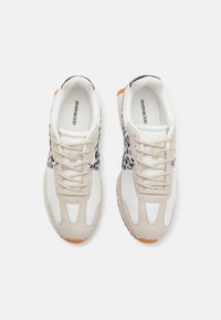 Beiget ja valkoiset tennarit teksturoidulla leopardikuviolla. Pyöristetty kärki, nauhakiristys ja kumipohja, jossa oransseja yksityiskohtia.