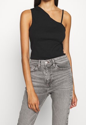 Black, asymmetrical tank top with a single strap and a ribbed texture. Paired with high-waisted, faded gray jeans.
