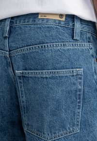 Denim jeans in een lichtblauwe kleur, met een klassiek vijf-pocket ontwerp, zichtbare stiksels en een crèmetint label met "EST. 1992" op de tailleband.