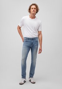 Light blue denim jeans with a slim fit, featuring five pockets and a faded finish. Paired with a plain white t-shirt and black and white sneakers.