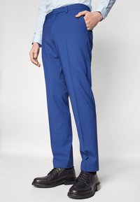 Blauwe op maat gemaakte broek met een soepele textuur, voorzien van een platte voorkant en zijzakken. Draagt met zwarte oxford schoenen.
