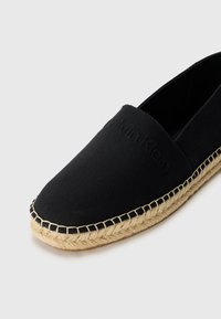 Crna kanvas espadrila sa slip-on dizajnom i đonom od jute konopca, s reljefnim logotipom brenda na gornjem dijelu i kontrastnim šavovima duž ruba.