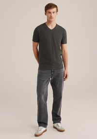 Sötétszürke V-nyakú póló rövid ujjakkal, elhalványult szürke farmernadrággal és világosszürke sportcipővel, amelyeken fehér részletek és minimalista dizájn található.