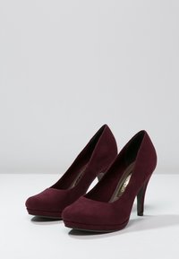 Bordeauxfärgade mockaklackar med rund tå, slät yta och plattformdesign. Smala stilettklackar ger ytterligare höjd.