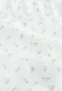 Witte stof met een fijne ribstructuur, voorzien van een delicate bloemenpatroon in lichtblauw en groen, met kleine bladeren die overal verspreid zijn.