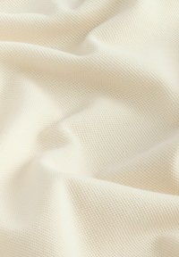 Vaaleanbeige neulottu kangas, jossa on tekstuuri ja avoin kudontamalli, esittäen pehmeitä, valuavia laskoksia ja sileää pintaa.