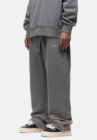 Grijze, oversized hoodie met een voorzak en afgeknipte mouwen, gedragen met bijpassende baggy joggingbroek met een klein logo op de linker bovenbeen.