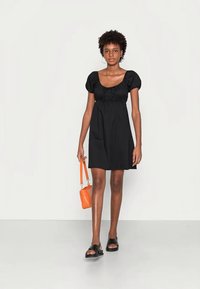 Vestido curto preto com mangas bufantes, corpete franzido e saia evasê. Combinado com uma pequena bolsa laranja e sandálias pretas.
