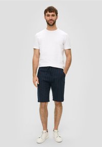 Marineblauwe gestreepte shorts met een trekkoord in de taille, gecombineerd met een eenvoudig wit T-shirt. Model staat met een hand in de zak, witte sneakers.