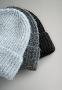 Drie gebreide mutsen in lichtgrijs, donkergrijs en zwart. Geribbelde textuur met een omgeslagen boordontwerp, gemaakt van zacht wollen materiaal.