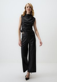 Zwarte faux leren outfit met een mouwloze drapering top en brede broekspijpen, die een gladde textuur en strakke lijnen tentoonstelt.