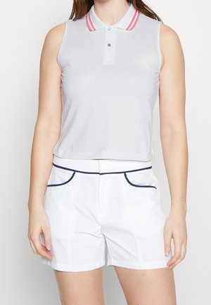 Biała koszulka polo bez rękawów z różowymi paskami na kołnierzyku, zestawiona z białymi szortami z granatowym paskiem na kieszeniach i pasie.