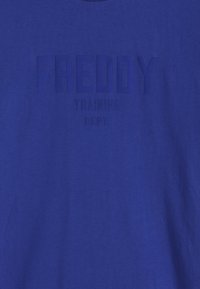 Camiseta azul de manga corta hecha de tela suave. Presenta texto en relieve "FREDDY" y "TRAINING DEPT." con un acabado mate en contraste.