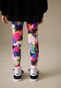 Leggings multicolores avec un imprimé graphique comprenant des éclaboussures de rose néon, vert et bleu, fabriqués en matériau extensible pour le confort.
