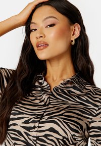 Blusa con stampa zebrate in beige e nero, caratterizzata da un colletto, chiusura con bottoni e una texture morbida e liscia. Il motivo audace contrasta con il colore del tessuto.