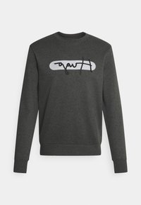 Un sweat-shirt gris foncé en tissu mélangé coton, avec un logo ovale blanc portant un texte en script noir à l'avant et des poignets côtelés.