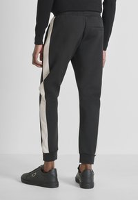 Zwarte sportbroeken met witte zijstrepen, elastische tailleband en een enkele achterzak. Glad materiaal en tapered leg ontwerp.