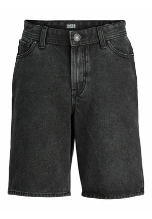 Garçon portant une chemise blanche à manches courtes par-dessus un t-shirt blanc, un short noir, des baskets blanches, des chaussettes et une casquette verte, debout sur un fond blanc.