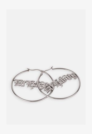 Orecchini a cerchio in argento con un design in carattere gotico appeso all'interno dei cerchi, caratterizzati da una finitura metallica lucida e una superficie liscia.