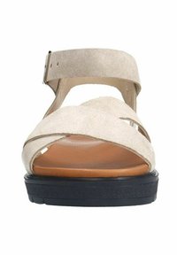 Beige suede sandaal met een kruislings ontwerp, verstelbare enkelband, bruine voetbed en zwarte gestructureerde zool. Platte constructie.