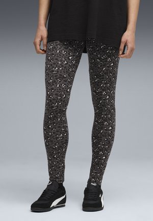 Zwarte leggings met een grijs luipaardprintpatroon, strakke pasvorm, rekbare stof, gecombineerd met zwarte sportschoenen met een witte accent.