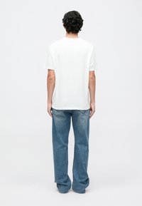Camiseta de algodón blanca con cuello redondo, manga corta y un corte holgado, combinada con jeans de mezclilla de pierna recta en azul claro.