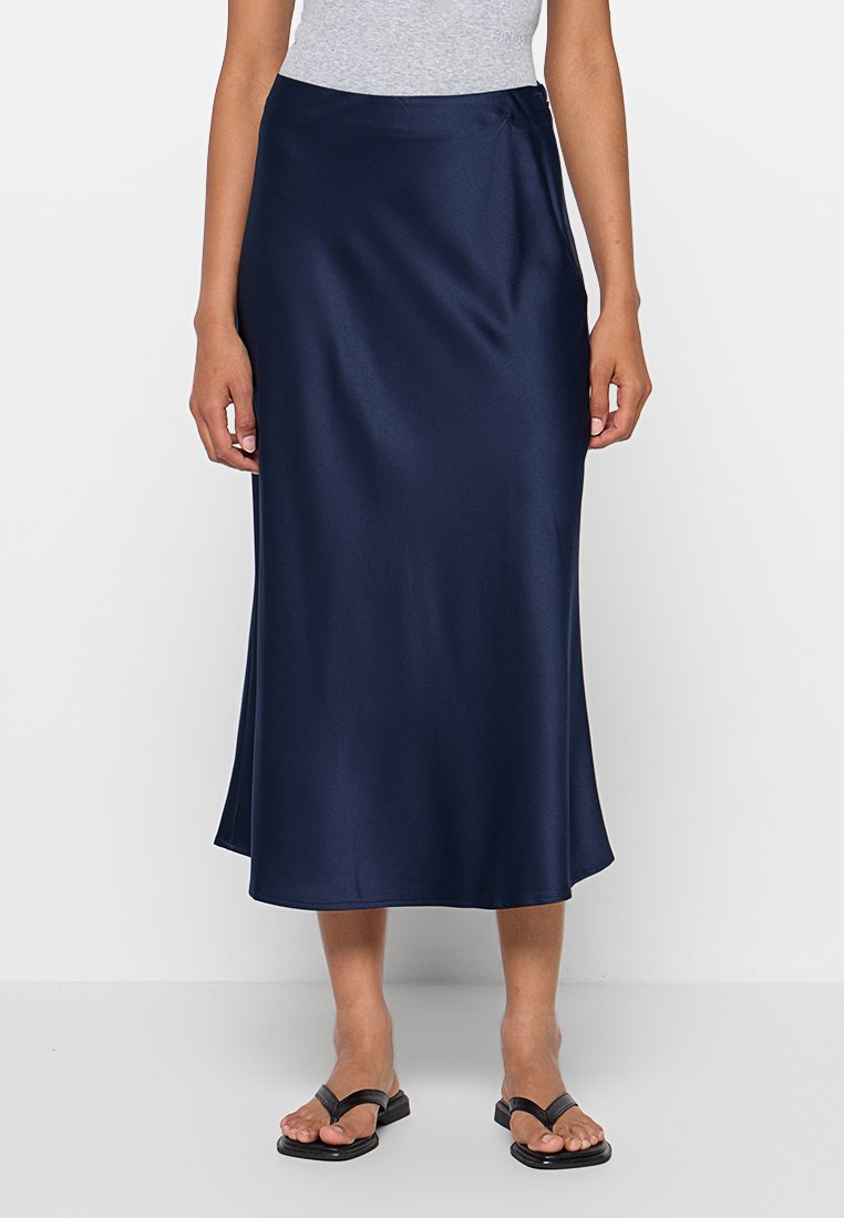 Jupe midi en satin bleu marine, avec une texture lisse, une fente sur le côté et une fermeture discrète. Associée à un haut gris et des sandales noires.