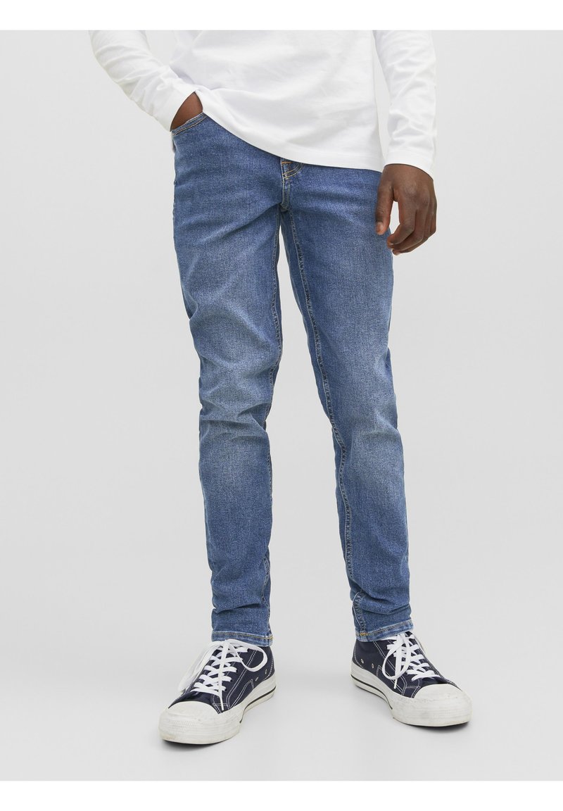 Jeans bleu délavé avec une coupe slim, dotés de cinq poches et de coutures décoratives, associés à des baskets navy et des lacets blancs.