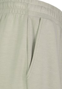 Hellgraue Hose aus weichem Stoff mit elastischem Bund, Seiten- und einer glatten, strukturierten Oberfläche.