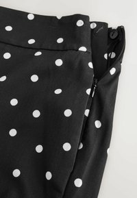 Tissu noir à pois blancs, avec une fermeture éclair partiellement ouverte et un bouton noir sur la ceinture.