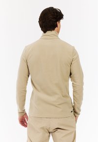 Beige fleece pullover med høj krave, lange ærmer og en subtil tekstur. Har et lille logo på den nederste del.