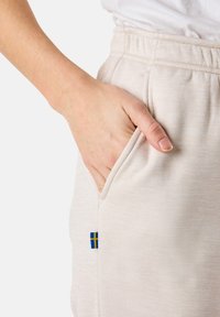 Ljusbeiga sweatshirtbyxor har en sidoficka och ett litet blå-gult flaggemblem. Tyget har en mjuk textur med en melerade mönster.