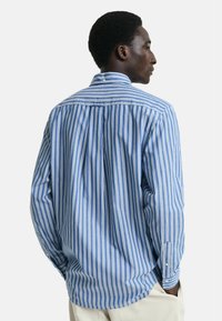 Camicia a maniche lunghe con righe verticali blu e bianche, realizzata in tessuto morbido. Presenta un colletto con bottoni e un polsino con un solo bottone.