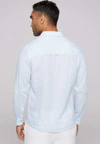 Camisa de manga larga azul claro hecha de lino con un diseño simple, que cuenta con un cuello abotonado y mangas enrollables con acentos de botón.