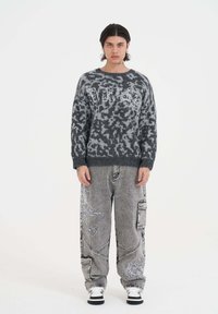 Grijze fuzzy trui met opvallende witte letters, gecombineerd met losse grijze spijkerbroeken met geborduurde ontwerpen en zakken. Zwart-witte sneakers.