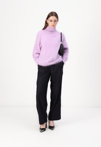 Lila puhasta turtleneck pulover v kombinaciji s črnimi širokimi hlačami s črtami in črnimi špicastimi petkami. Majhna črna torbica kot dodatek.