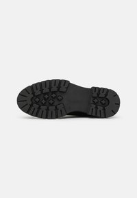 Black rubber shoe sole featuring a rugged tread pattern with deep grooves and pivot points for traction, designed for stability and grip.