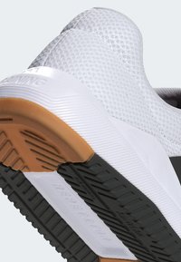 Hvid sportsko med en struktureret mesh-overdel, en solid gummisål med en sort detalje og hæl i gummigummi, designet til komfort og ydeevne.
