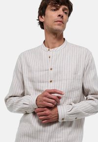 Chemise à rayures claires avec un col mao, des boutons en bois et une poche poitrine ; fabriquée dans un tissu riche en textures.