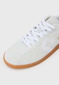 Light gray suede sneaker with white laces, rubber sole, and white side accents, featuring a star logo and minimalistic design.