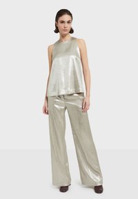 Srebrna metalik bezrukava bluzica i široke hlače. Glatka tekstura, ležeran kroj, minimalistički dizajn, bez vidljivih akcenata ili uzoraka.
