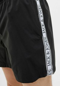 Zwarte zwembroek met een logo-strook aan de zijkant met "JACK & JONES" in het wit. Gemaakt van lichtgewicht stof met een elastische tailleband.