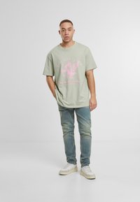 Světle zelené oversized tričko s růžovým grafickým textem a ilustrací. Spárované s vybledlými modrými džíny a bílými teniskami.